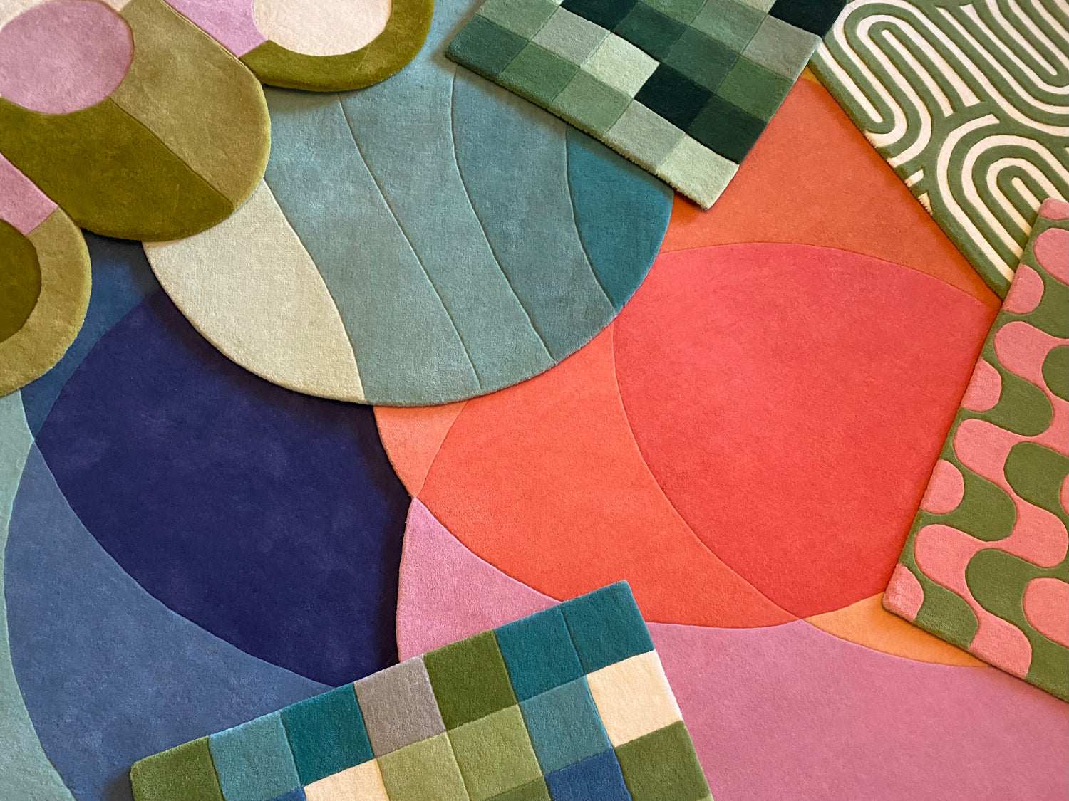 A photograph showcasing multiple overlapping, hand-tufted wool rugs designed in Stockholm, featuring vibrant shades of red, orange, blue, turquoise, green, and pink in striking modern abstract patterns. These carpets are arranged to highlight their harmonious color combinations and are suitable for various home spaces—including lounges, bedrooms, dining rooms, living rooms, bathrooms, kitchens, and even as doormats—adding both style and comfort to any interior. Ett fotografi som visar flera överlappande, ha